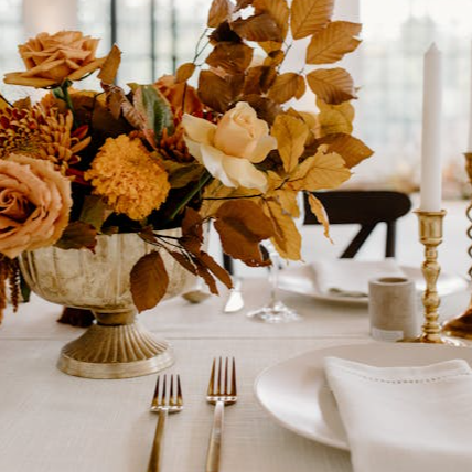 Elegant floral composition in vase placed on white table with ceramic plates and golden cutlery during festive banquet