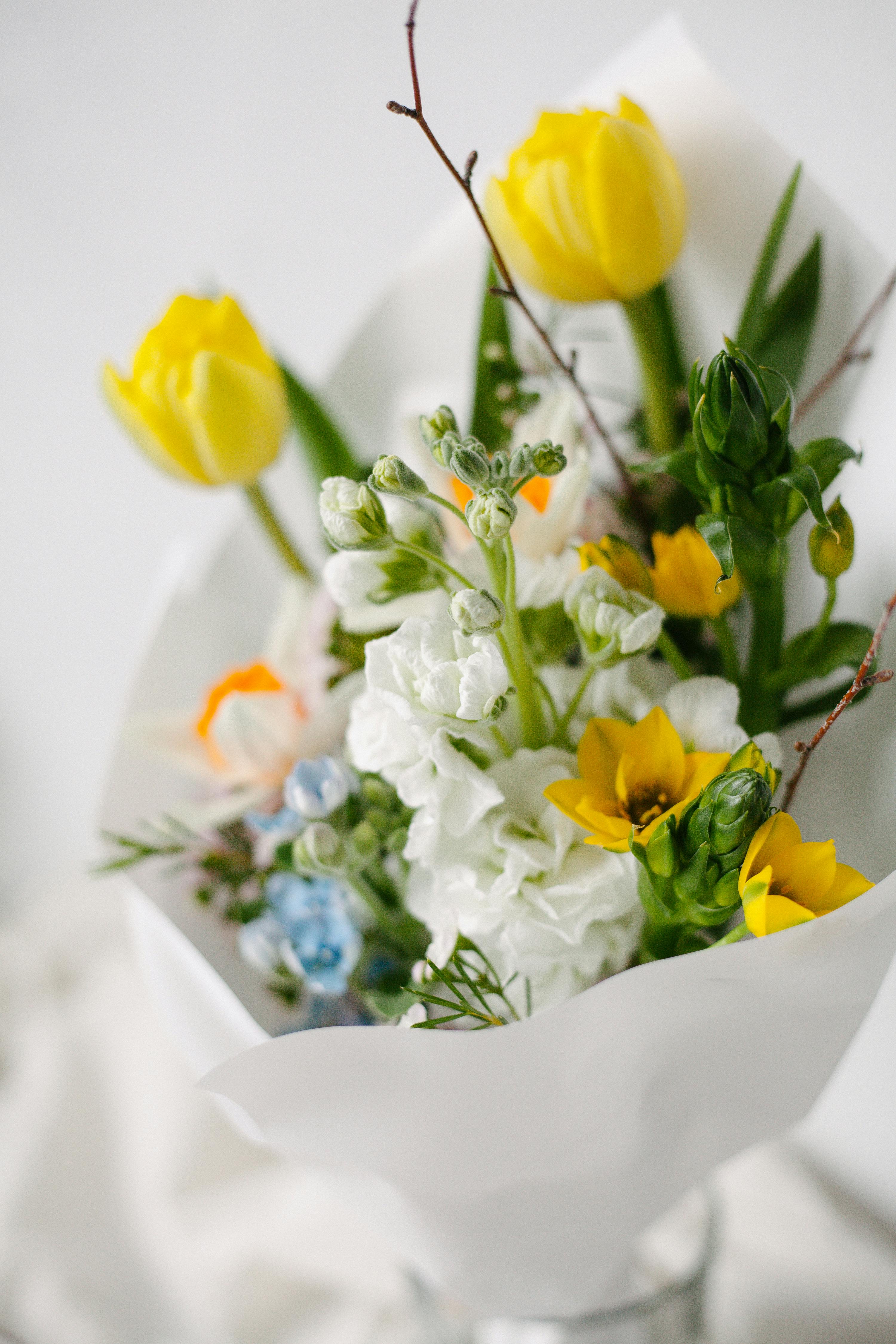 Elegant bouquet with yellow tulips and white blossoms in soft lighting.