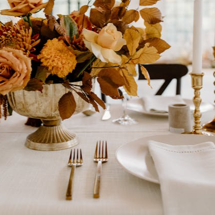 Elegant floral composition in vase placed on white table with ceramic plates and golden cutlery during festive banquet